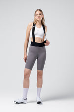 Woman wearing Gobik X Bib Short in gray with white sports bra and cycling shoes