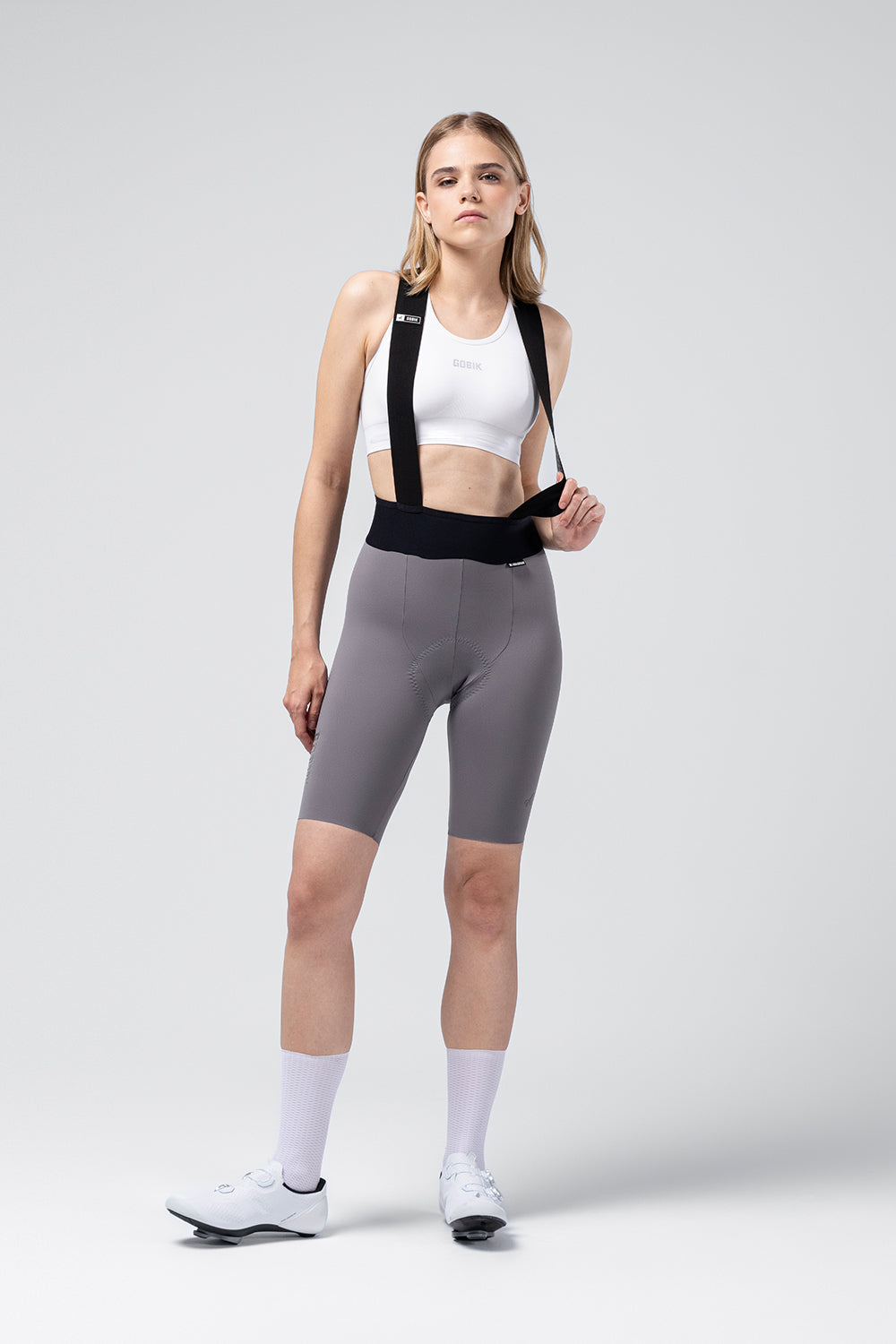Woman wearing Gobik X Bib Short in gray with white sports bra and cycling shoes