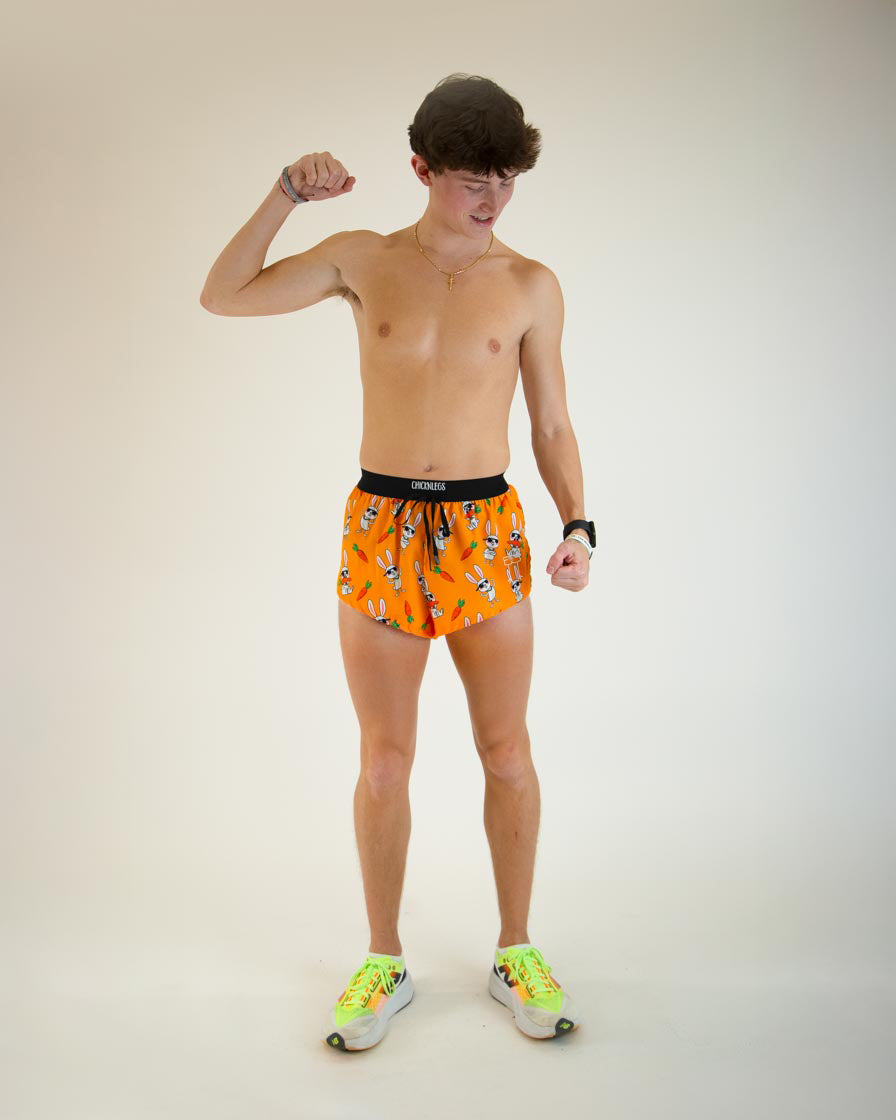Male model wearing ChicknLegs orange Bad Bunny split running shorts flexing pose