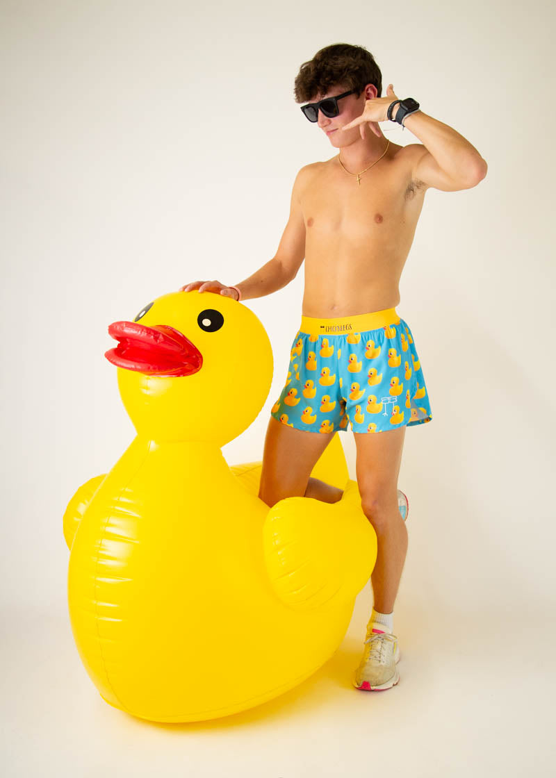 Man wearing ChicknLegs rubber ducky print swim shorts with giant inflatable duck