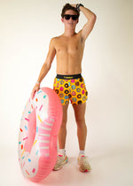 Man wearing yellow ChicknLegs donut print shorts holding inflatable donut ring