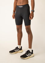 Man wearing black ChicknLegs 8-inch half tights with Adidas sneakers on neutral background