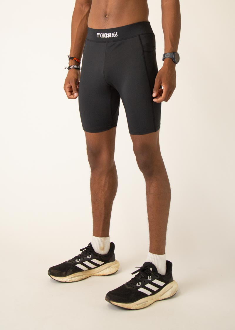 Man wearing black ChicknLegs 8-inch half tights with Adidas sneakers on neutral background