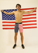 Man wearing ChicknLegs USA flag pattern compression shorts holding American flag