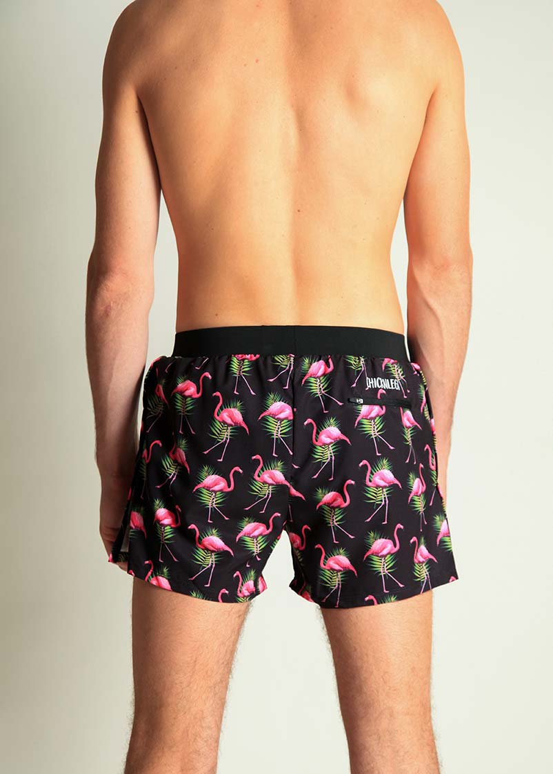 Back view of man wearing black swim shorts with pink flamingo pattern