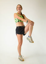 Woman wearing green pickle-patterned sports bra doing stretching exercise pose