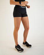 Woman wearing black ChicknLegs 3-inch compression shorts with Nike sneakers on white background
