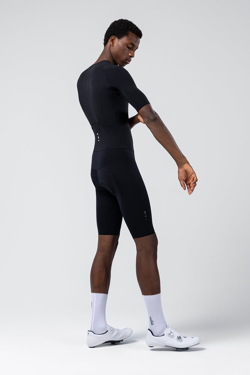 Male model wearing black Gobik Integral Hudson cycling kit with white shoes