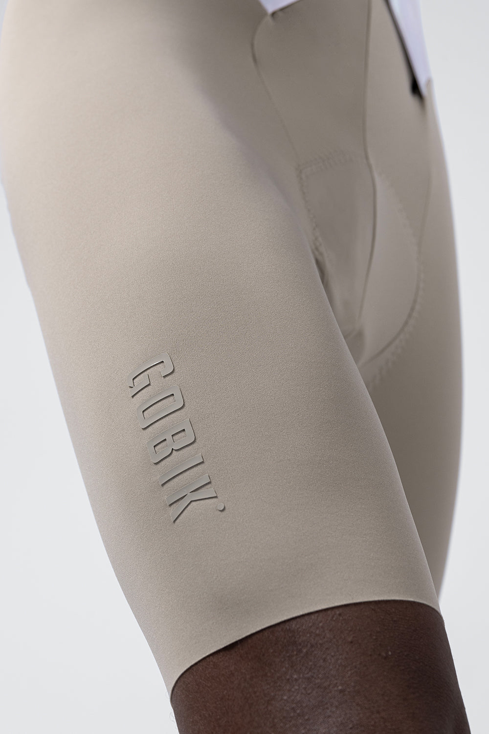 Close-up of Gobik branded bib shorts leg in beige sand color with embossed logo detail
