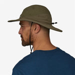 Man wearing olive green Patagonia Quandary Brimmer hat with chin strap, side profile view