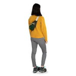 Woman wearing Osprey Daylite green waist pack crossbody over yellow sweater, rear view