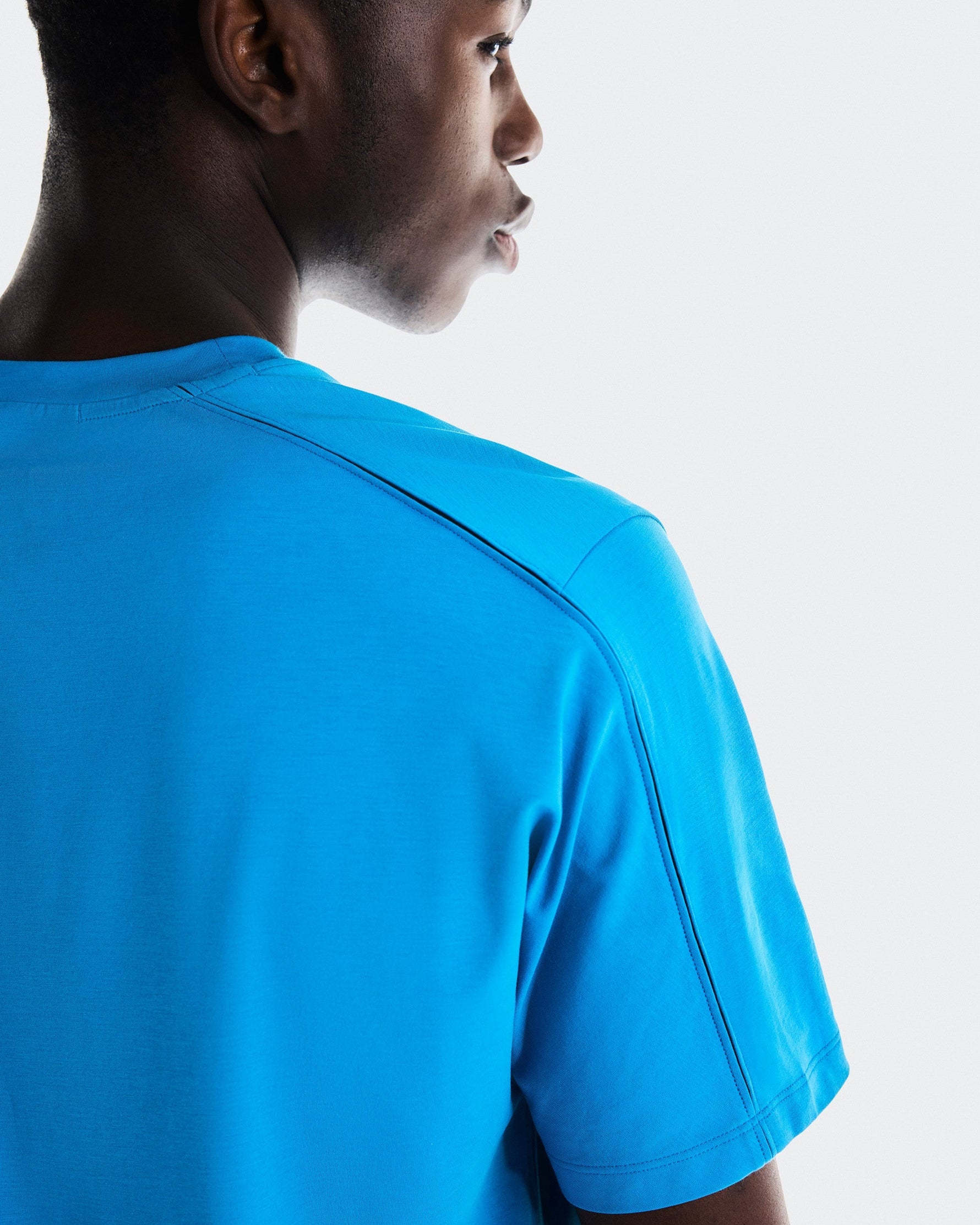 Man wearing bright blue On Focus-T athletic shirt, back view studio shot