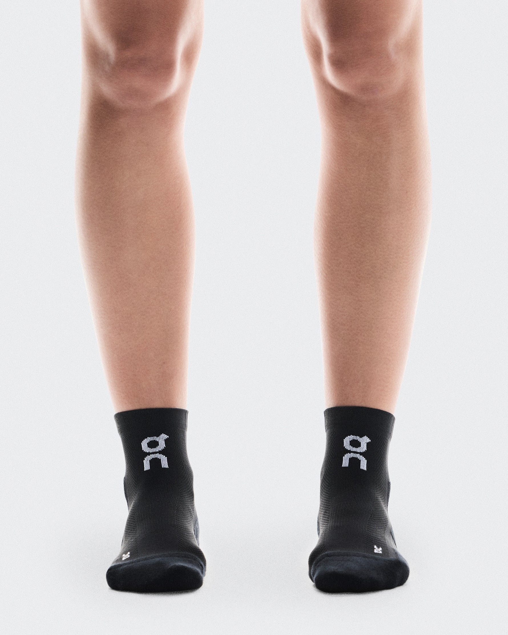 Black On running socks with white logo worn on legs against clean background