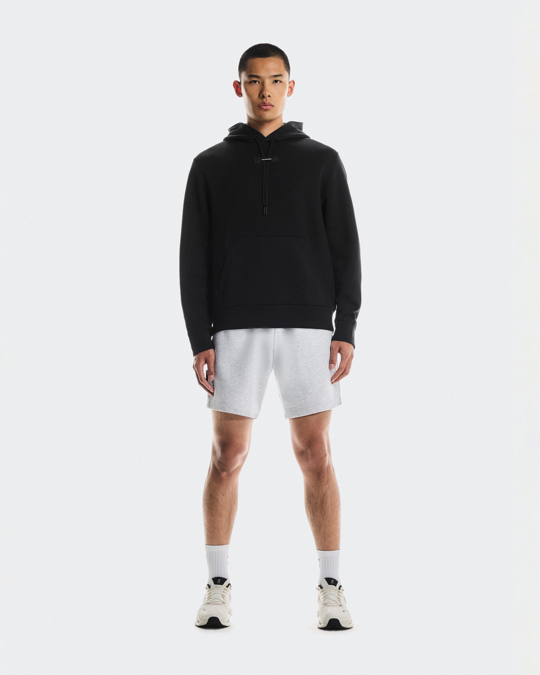 Man wearing black On Focus Tech Hoodie with gray shorts and white sneakers