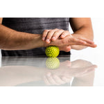 Person using green spiky massage ball on forearm for muscle therapy