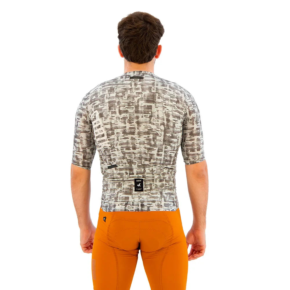 Back view of cyclist wearing grey patterned jersey with orange shorts