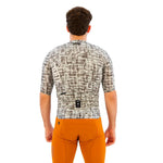 Back view of cyclist wearing grey patterned jersey with orange shorts