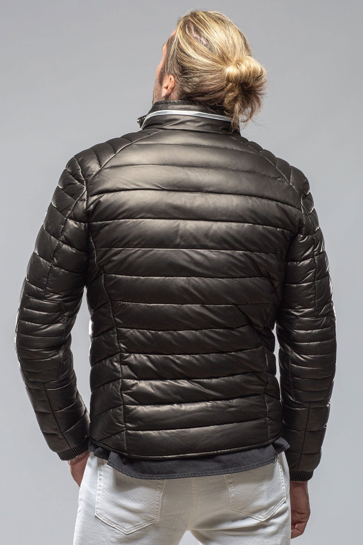 Man wearing black quilted puffer jacket shown from behind on gray background