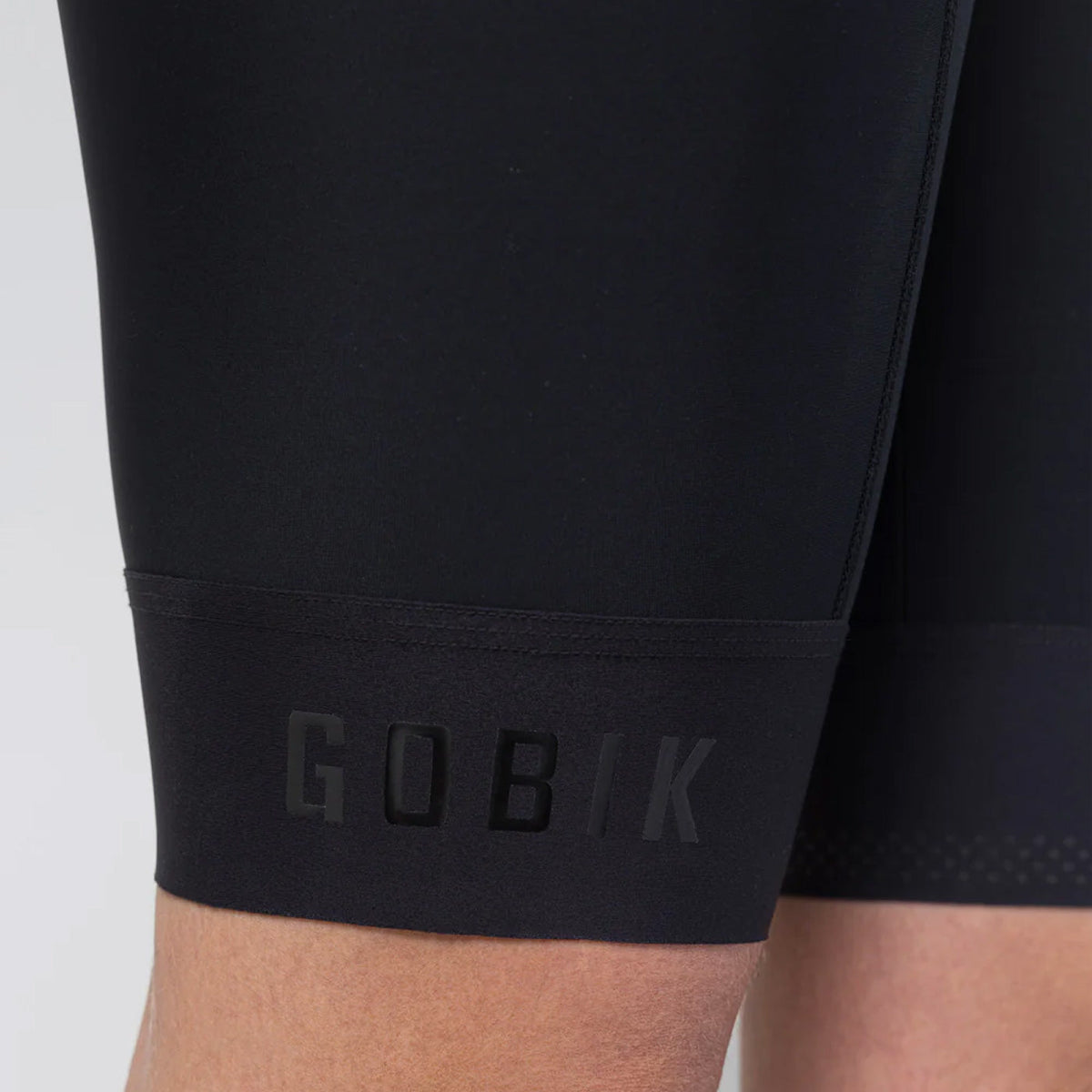 Close-up leg hem detail of Gobik Limited 6.0 black bib shorts showing GOBIK branded gripper band
