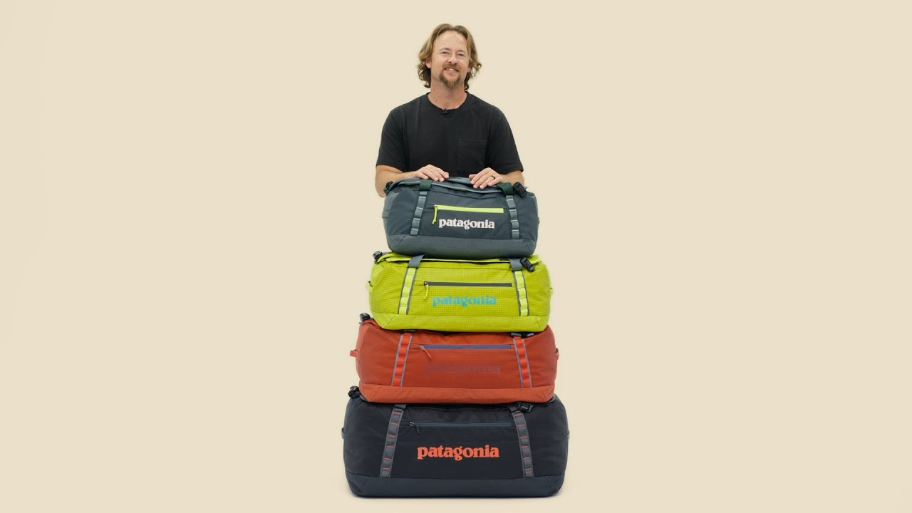 Man with stacked Patagonia Black Hole duffel bags in multiple colors including Hot Ember