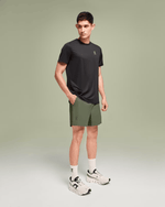 Man wearing On Essential Shorts in taiga green with black tee and white sneakers