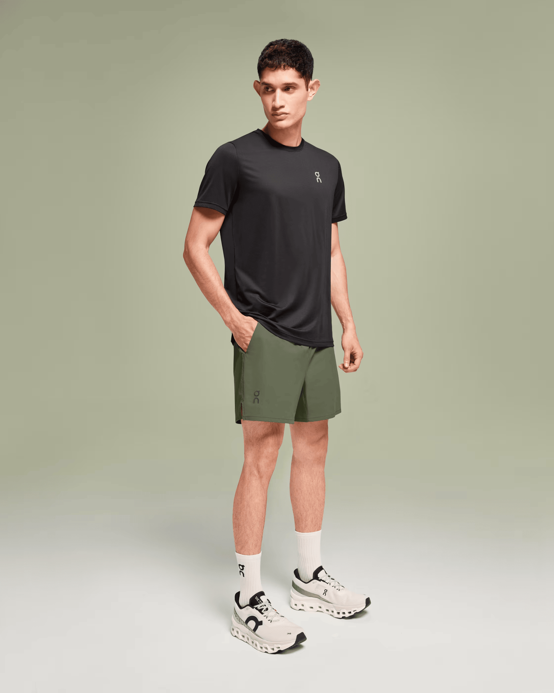Man wearing On Essential Shorts in taiga green with black tee and white sneakers