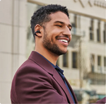 Man wearing black Shokz OpenDots ONE earbuds while smiling outdoors