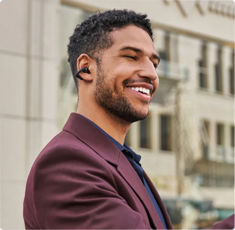 Man wearing black Shokz OpenDots ONE earbuds while smiling outdoors