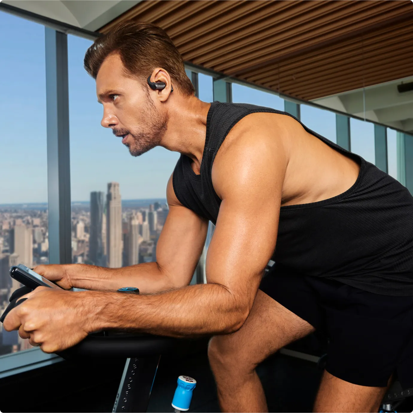 Man wearing black Shokz OpenFit Pro earbuds while exercising on stationary bike