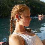 Woman wearing red AfterShokz OpenRun bone conduction headphones by water