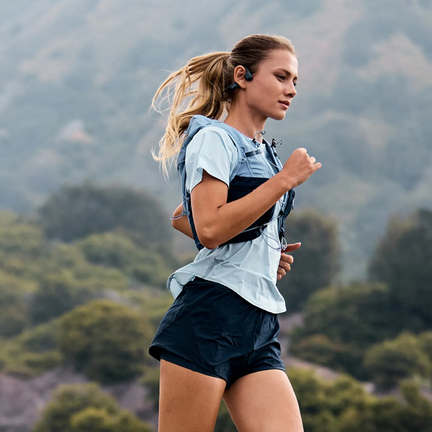 Woman running outdoors wearing black Shokz OpenRun Pro 2 bone conduction headphones