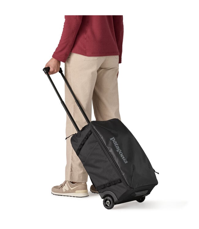 Person rolling Patagonia Black Hole MLC Wheelie 34L black luggage using telescoping handle