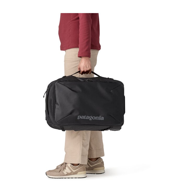 Person carrying Patagonia Black Hole MLC Wheelie 34L black bag by top handle, side view