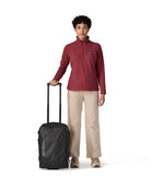Woman in red Patagonia fleece standing beside black Patagonia Black Hole MLC Wheelie 34L luggage