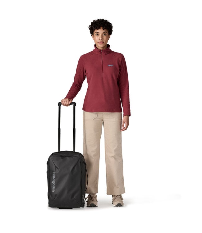 Woman in red Patagonia fleece standing beside black Patagonia Black Hole MLC Wheelie 34L luggage