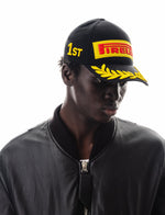 Model wearing black Pirelli branded cap with yellow laurel wreath and 1st embroidery
