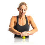 Woman using green TriggerPoint MobiPoint massage ball on white surface with hands positioned above