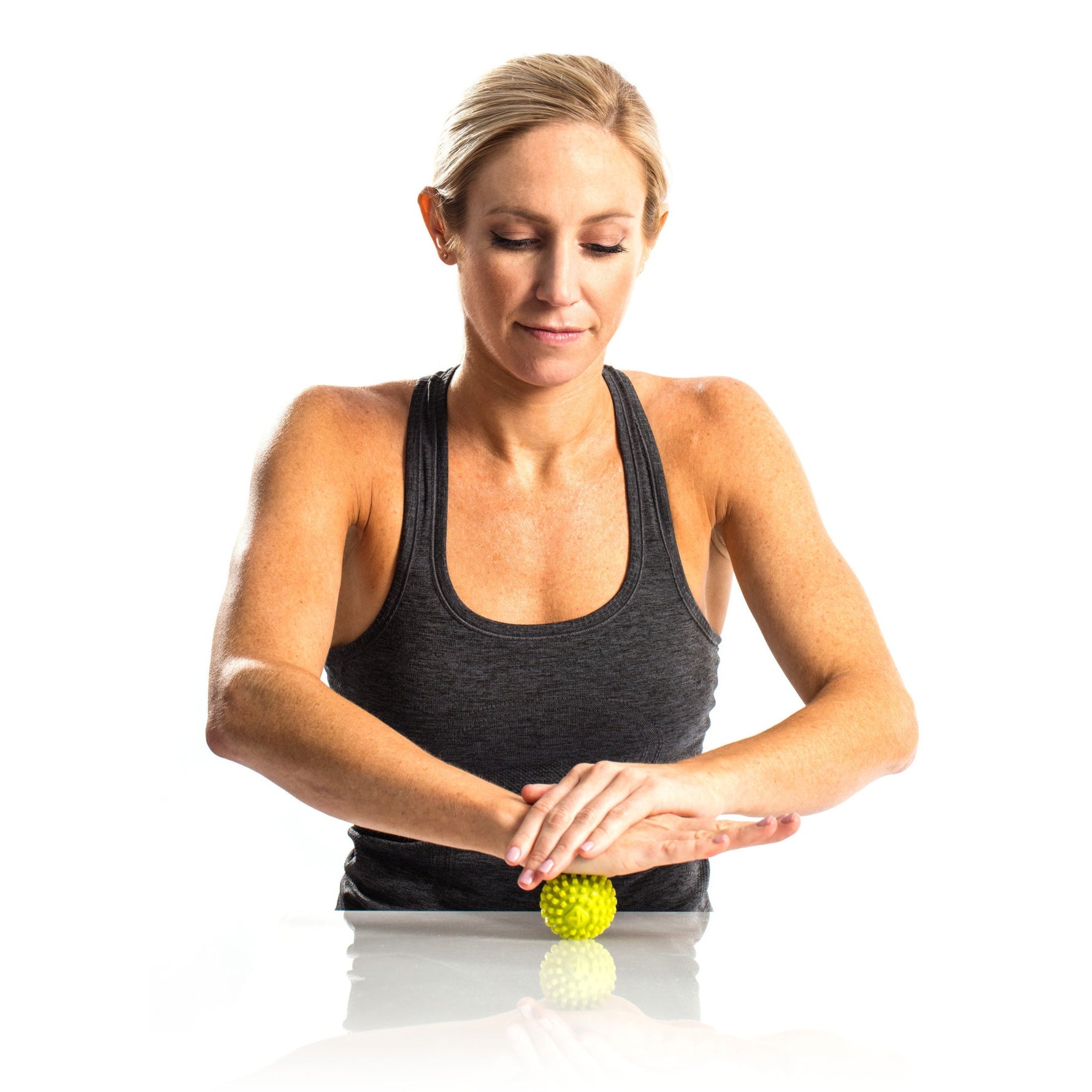 Woman using green TriggerPoint MobiPoint massage ball on white surface with hands positioned above
