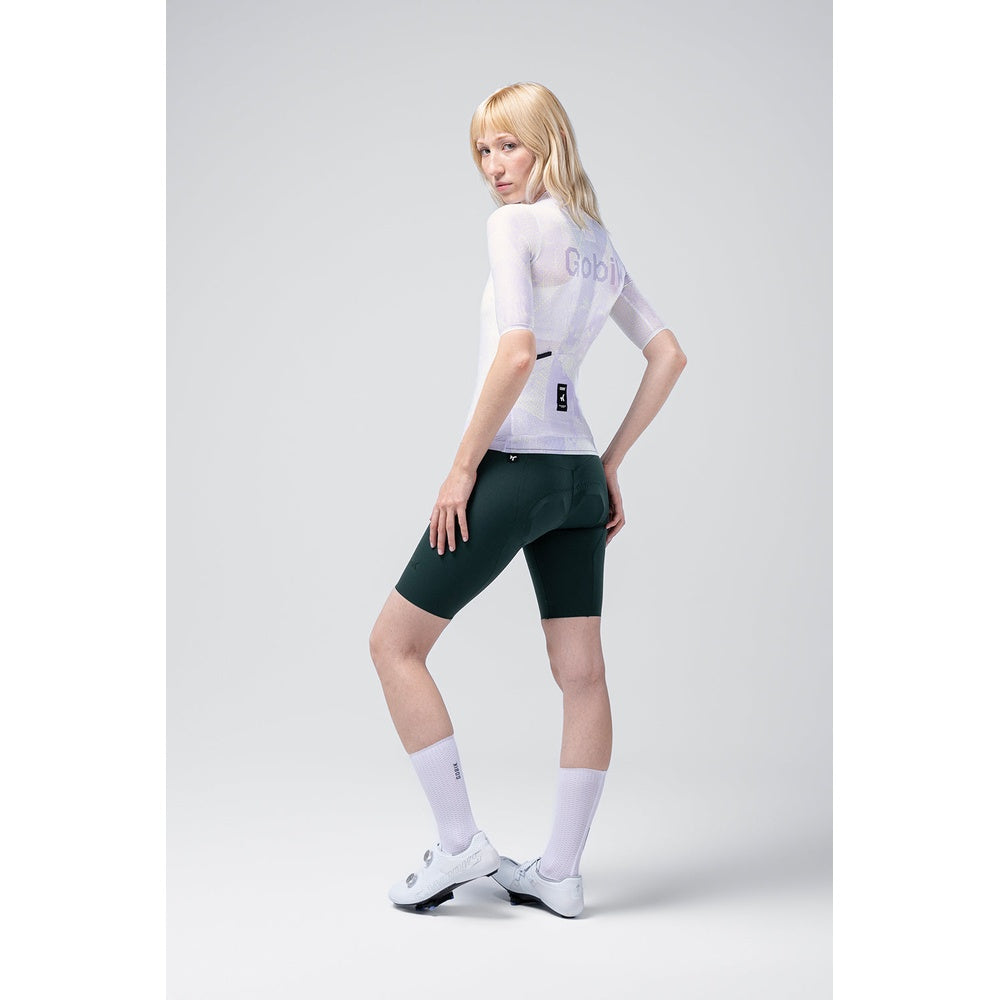Woman wearing white Gobik Miami Attitude jersey with green cycling shorts in studio setting