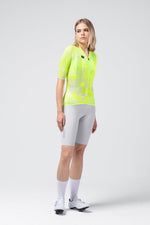 Woman wearing bright neon yellow Gobik Carrera 3.0 cycling jersey with gray shorts