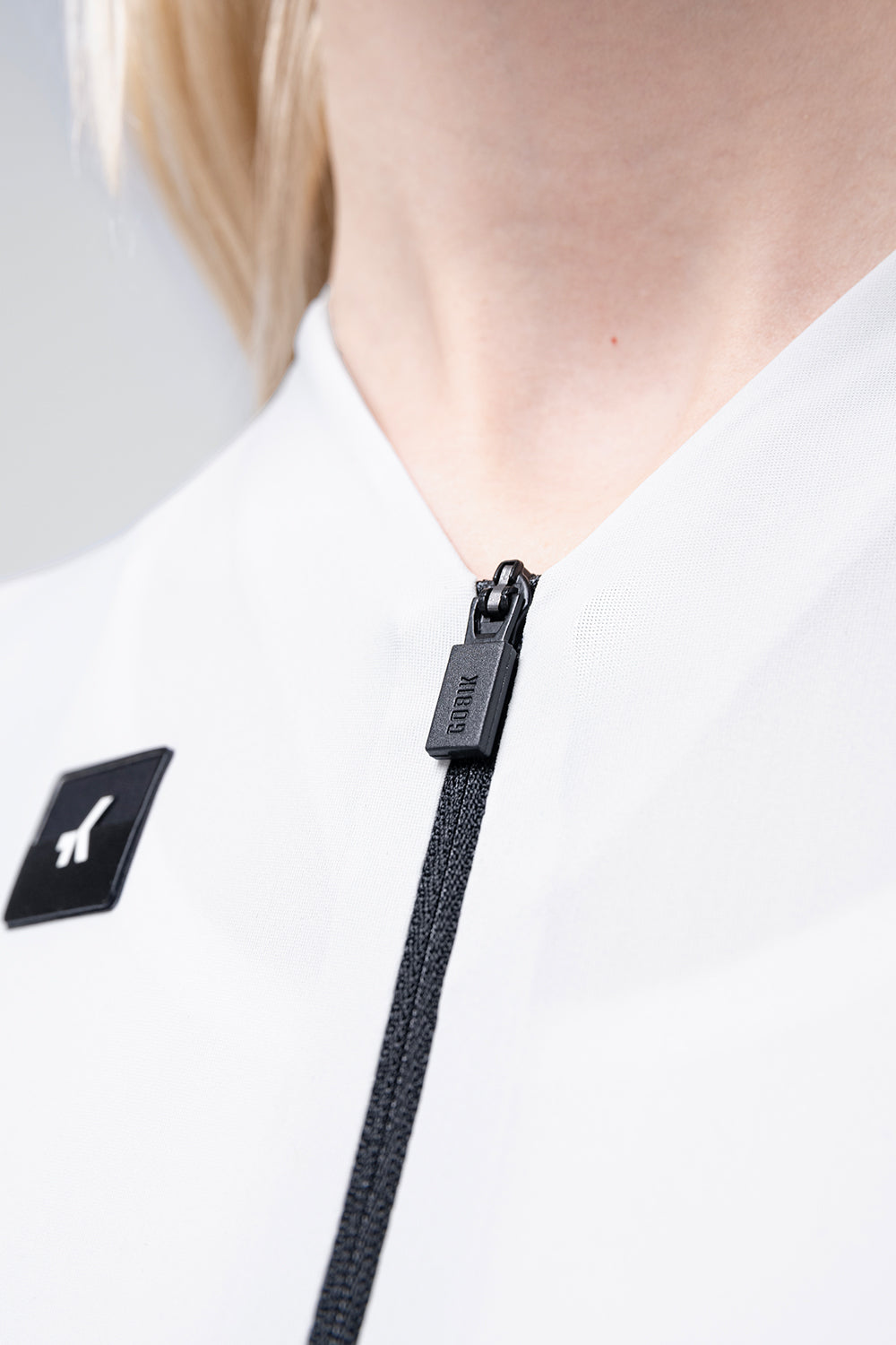Close-up detail of Gobik CX Solid cycling jersey in Empire white showing zipper and brand patch