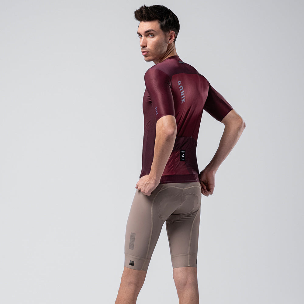 Man wearing Gobik Magnitude burgundy cycling jersey with gray shorts, studio photography