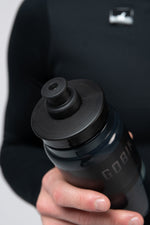 Hand holding black Gobik Fly water bottle with push-pull cap against dark background