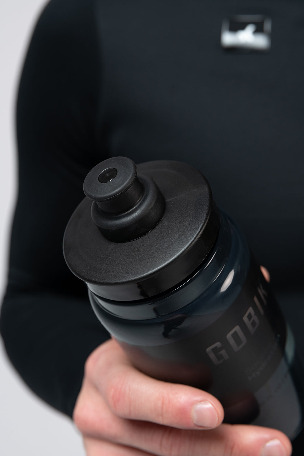 Hand holding black Gobik Fly water bottle with push-pull cap against dark background