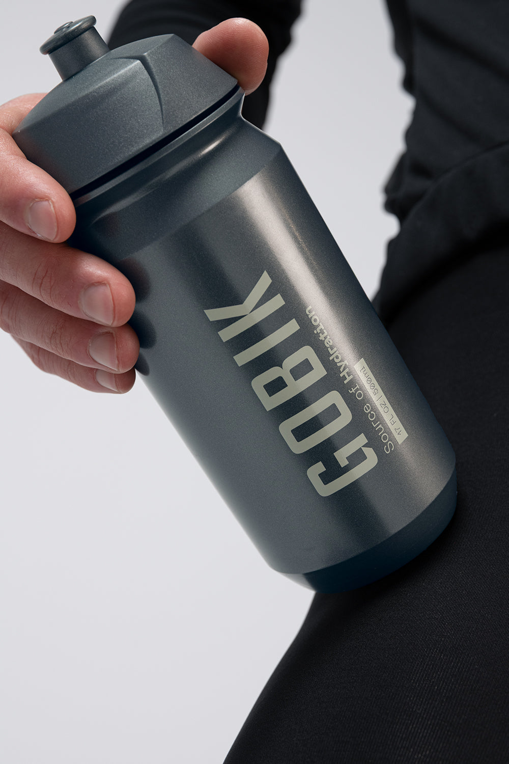 Hand holding Gobik dark grey water bottle with logo against white background