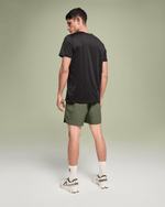 Man wearing On Essential Shorts in taiga green with black t-shirt and white sneakers