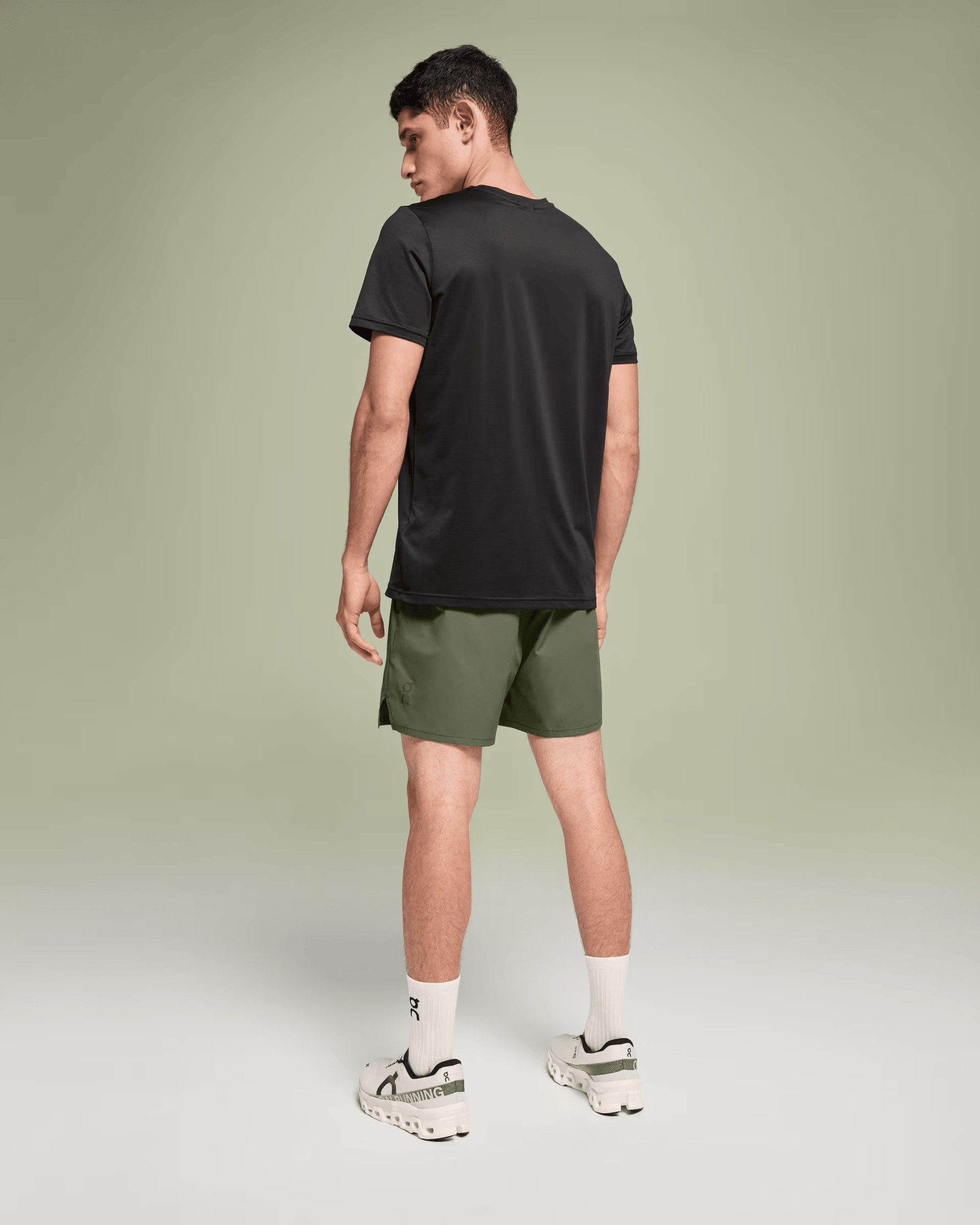 Man wearing On Essential Shorts in taiga green with black t-shirt and white sneakers