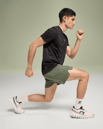 Male model running in On Essential Shorts in taiga green color with black shirt