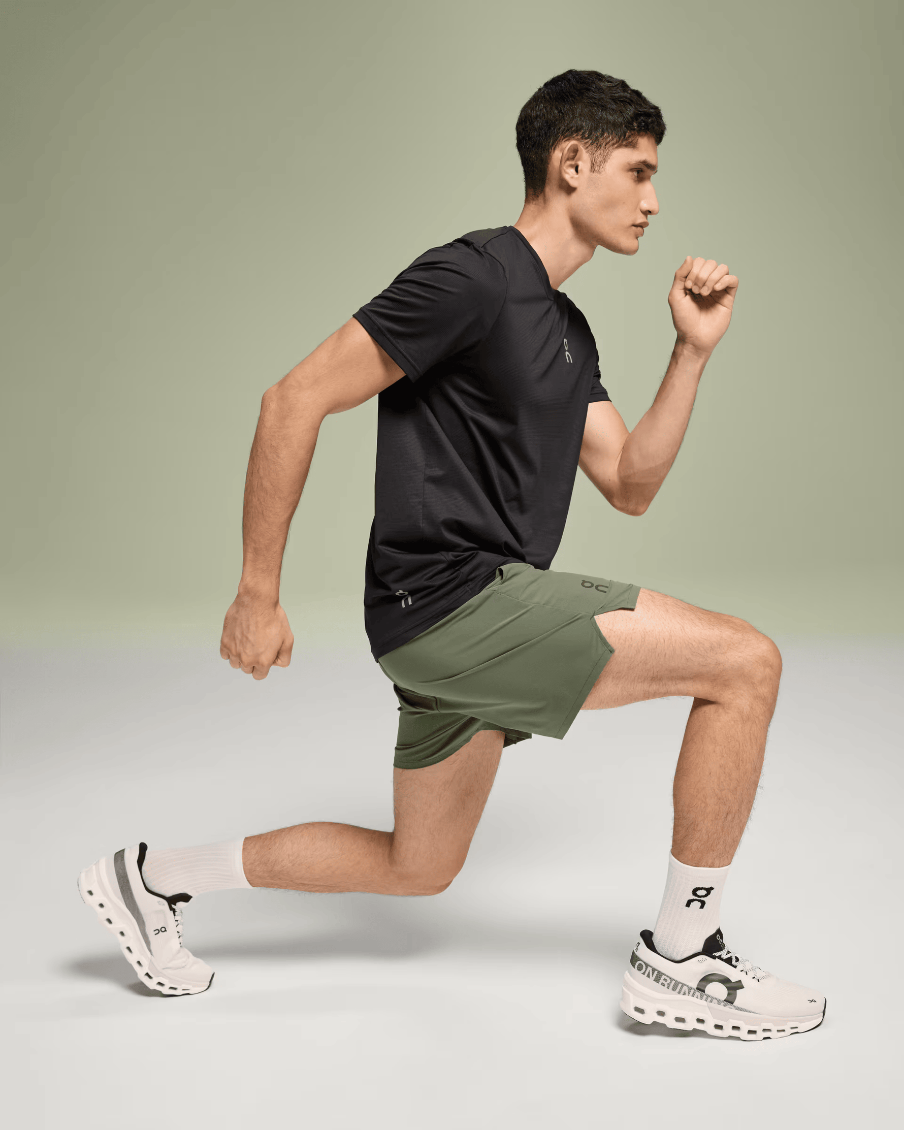 Male model running in On Essential Shorts in taiga green color with black shirt